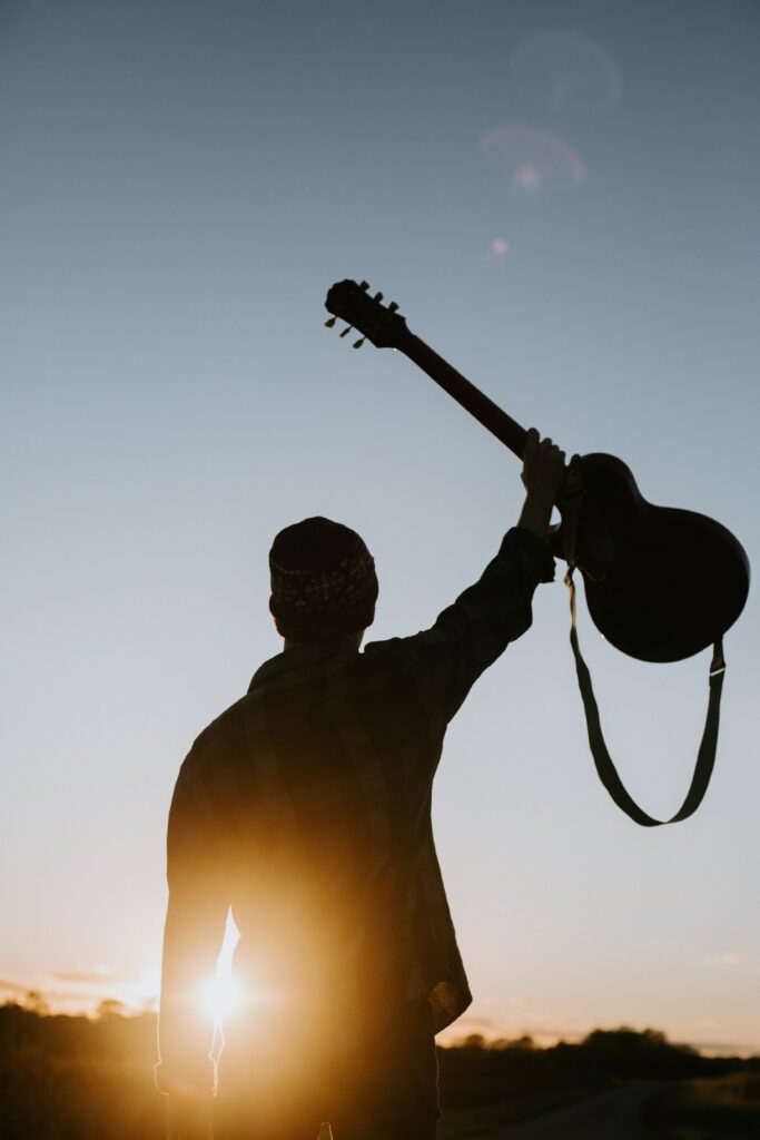 Man holding guitar high up in the air against a sunset